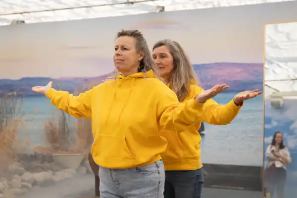 Zwei Frauen in gelben Hoodies tanzen vor einer Wasserlandschaft bei "Bewegte Bilder".
